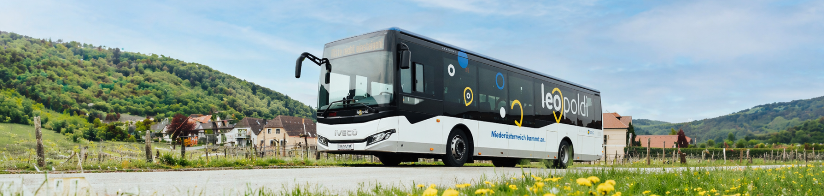LEOpoldi Reginalbusverkehr, © NÖVOG/Grojer, KI optimiert Bus mit der Aufschrift 'LEOpoldi' fährt auf einer Landstraße vor einer hügeligen Landschaft mit Häusern und Wiesen