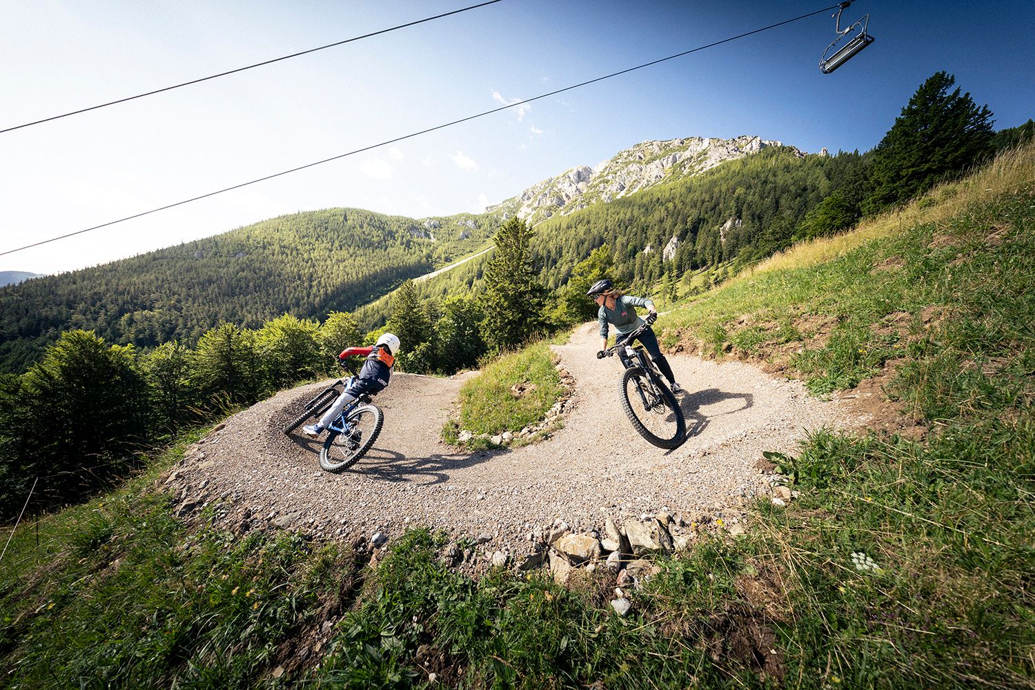 Alpen Bikepark Schneeberg im Sommer. Zwei Rider fahren eine Kehre hinunter, im Hintergrund trohnt der Schneeberg.