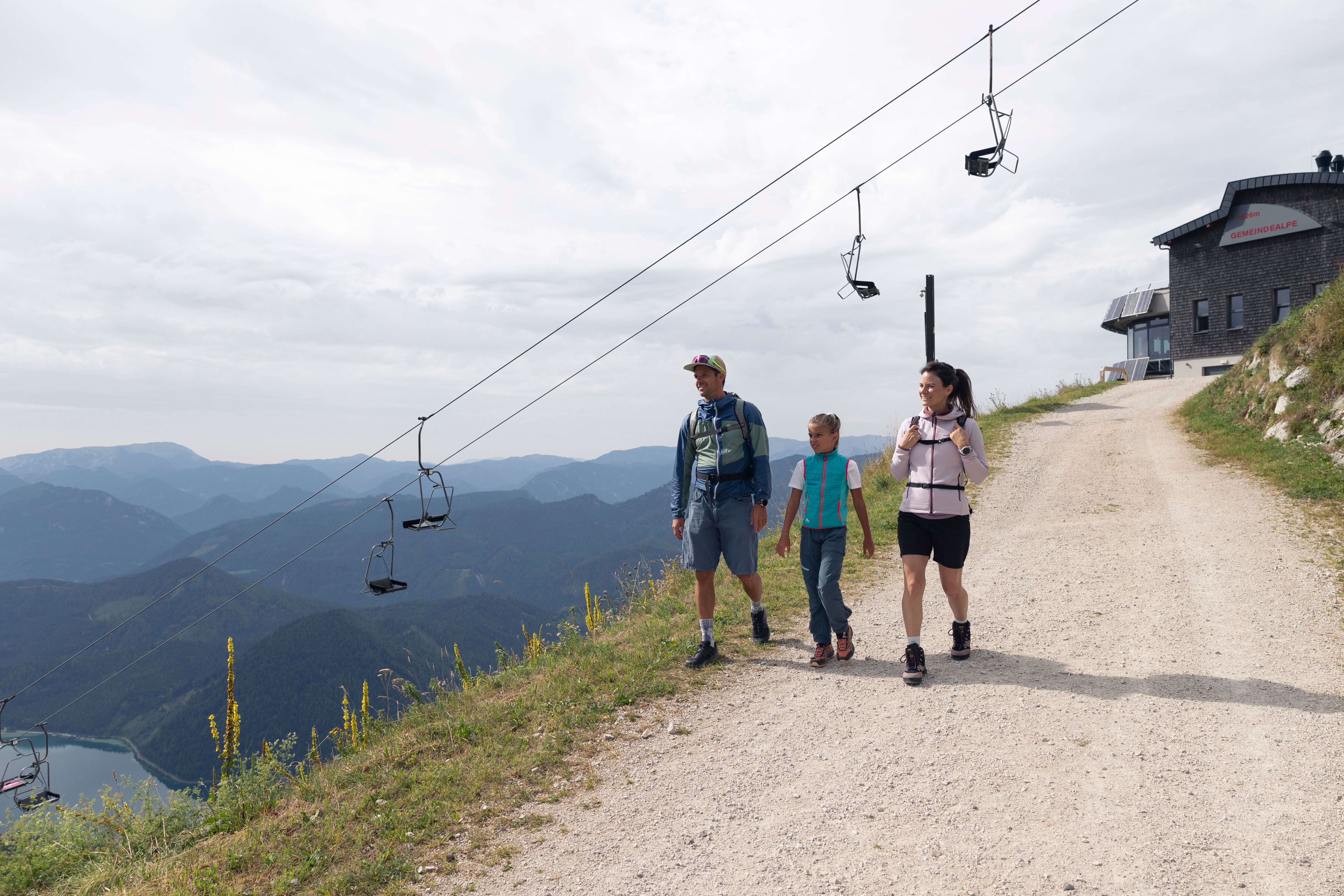 Gemeindealpe Mitterbach im Sommer. Familie wandert von der Bergstation hinunter. Im Hintergrund sieht man die Sesselbahn und den Erlaufsee.