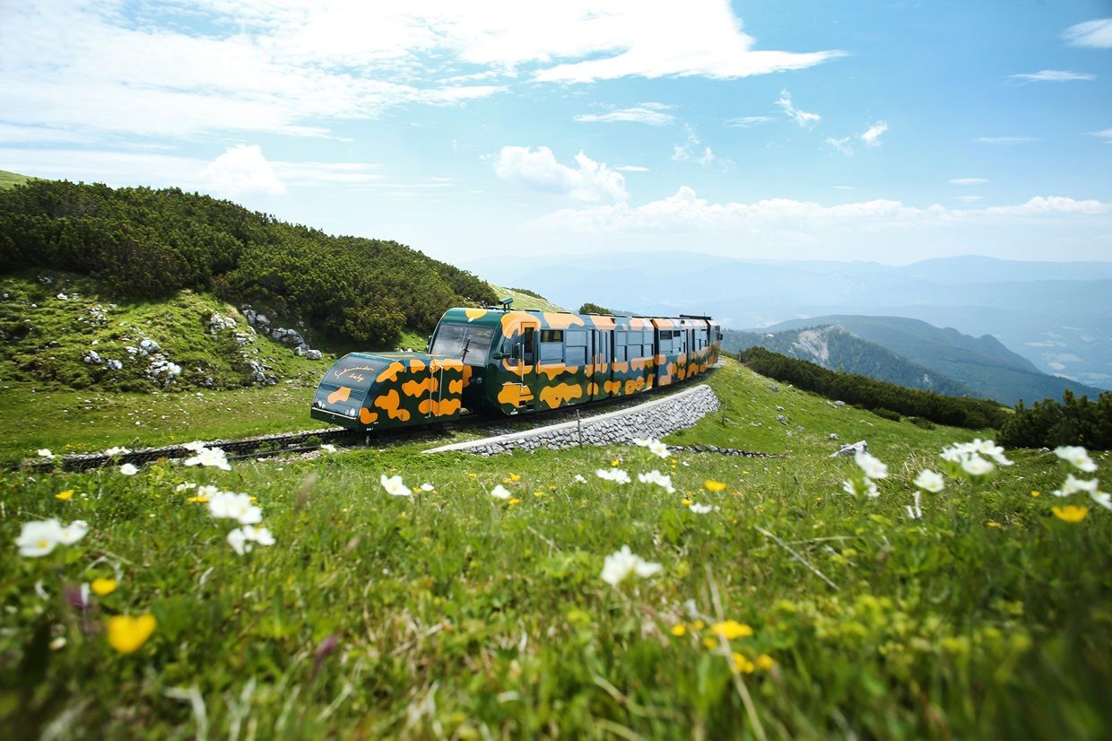 Salamanderzug der Schneebergbahn bei Fahrt Richtung Bergbahnhof. Im Hintergrund sieht man das alpine Panorama der umliegenden Berge.