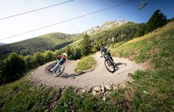Alpen Bikepark Schneeberg im Sommer. Zwei Rider fahren eine Kehre hinunter, im Hintergrund trohnt der Schneeberg.
