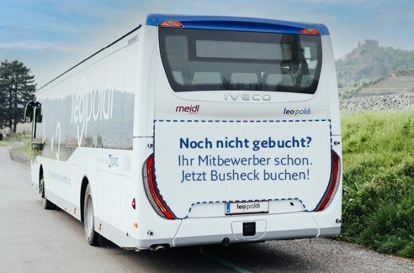 Heckansicht eines wei&szlig;en Reisebusses mit der Aufschrift 'Noch nicht gebucht? Ihre Mitbewerber schon. Jetzt Busheck buchen!'